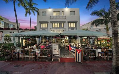 Hotel exterior at dusk with outdoor dining area, palm trees, and lit façade along a lively street at Hotel Chelsea, A South Beach Group Hotel.
