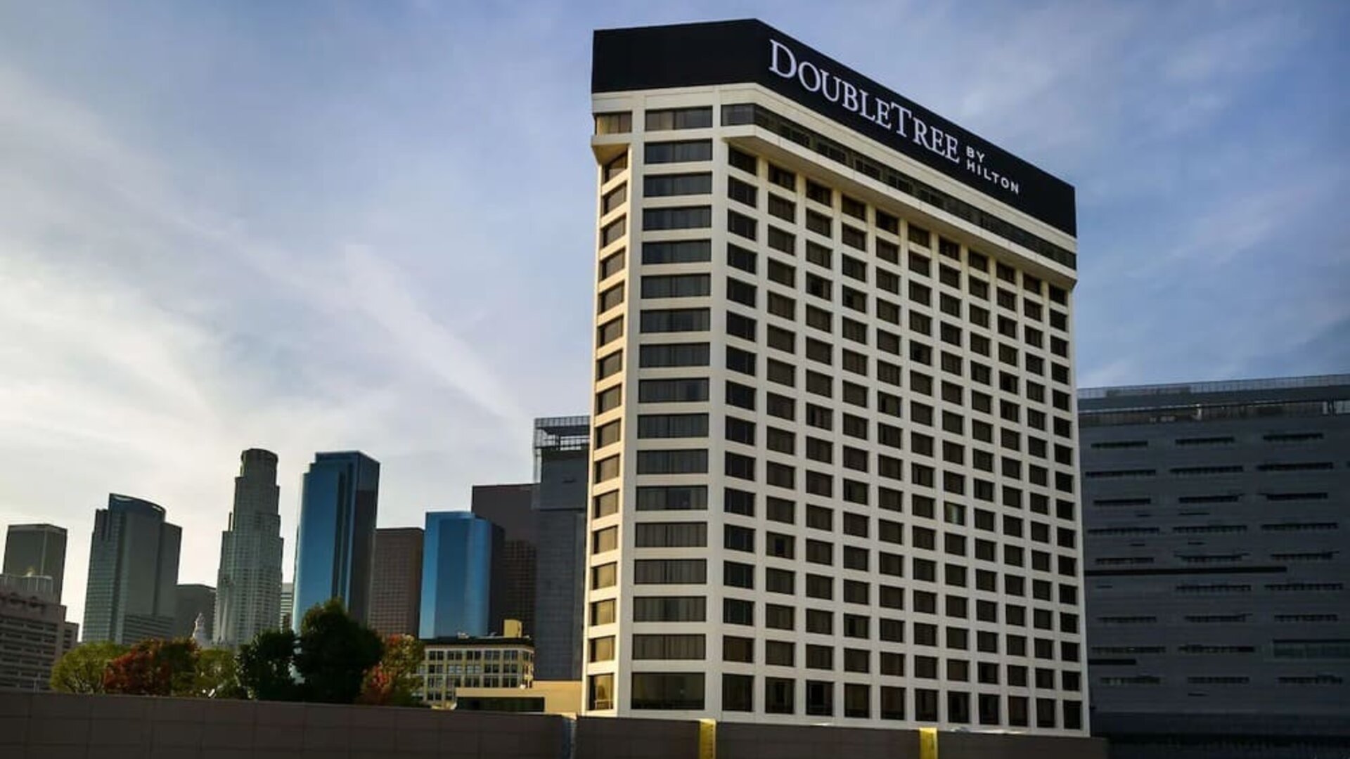 Exterior view of tall hotel building with DoubleTree signage and city skyline backdrop at DoubleTree By Hilton Los Angeles Downtown.