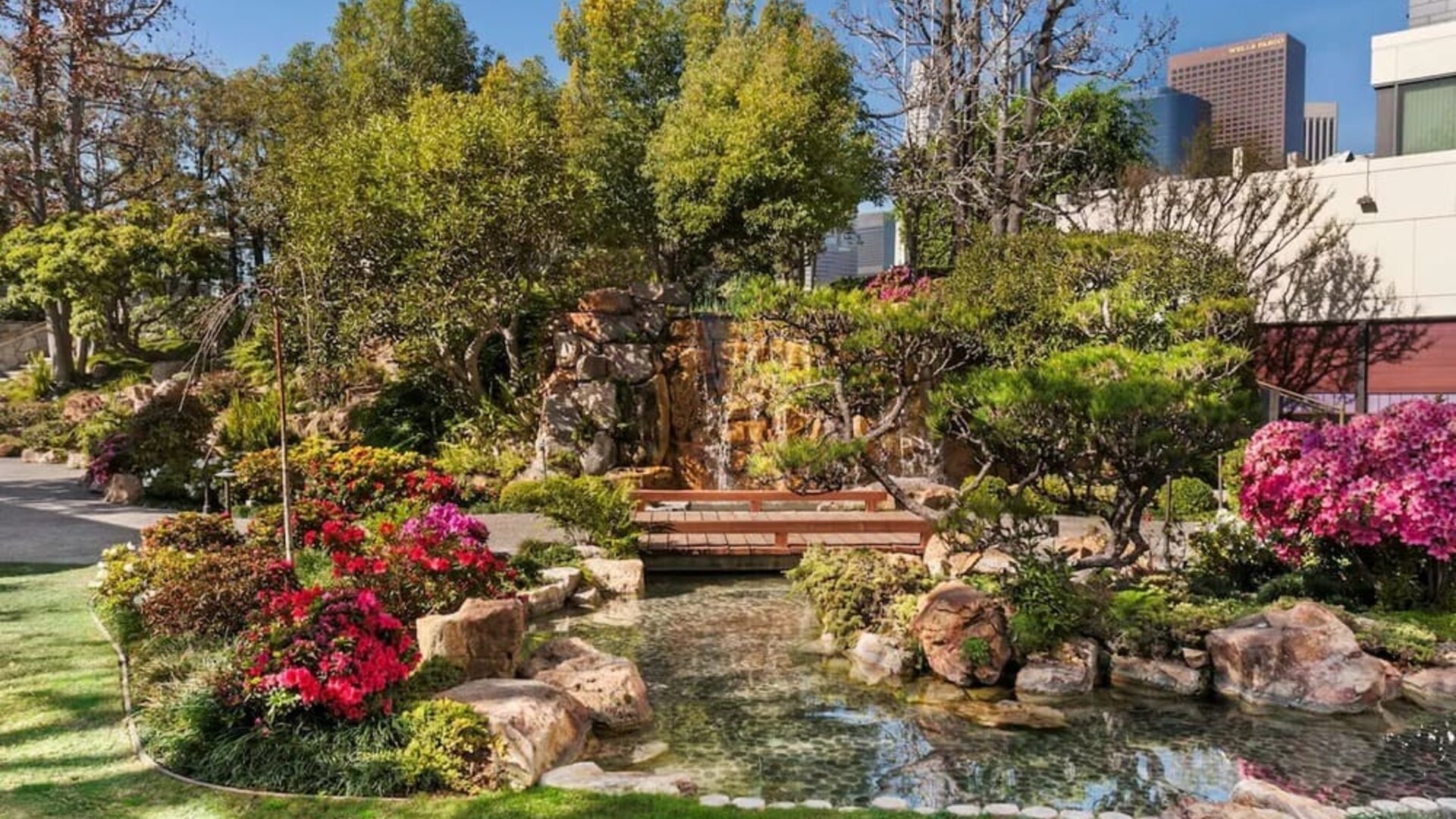 Landscaped garden with pond, wooden bridge, rocks, and colorful flowering plants at DoubleTree By Hilton Los Angeles Downtown.