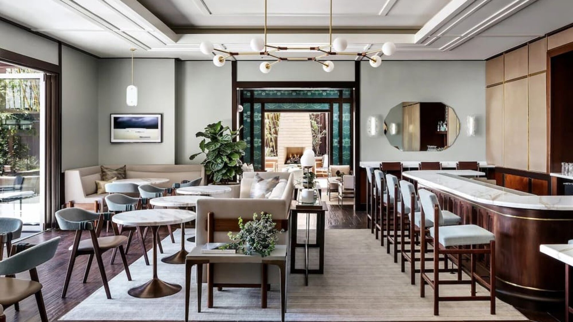 Elegant dining area with marble tables, bar seating, modern chandelier, and soft neutral tones at The Ambrose Hotel Santa Monica.