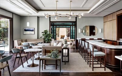 Elegant dining area with marble tables, bar seating, modern chandelier, and soft neutral tones at The Ambrose Hotel Santa Monica.