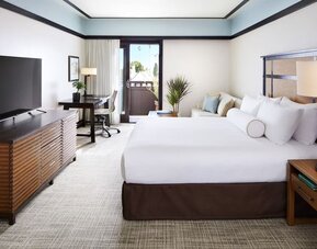 Bright guest room with king bed, desk, TV console, and balcony access with outdoor seating at The Ambrose Hotel Santa Monica.