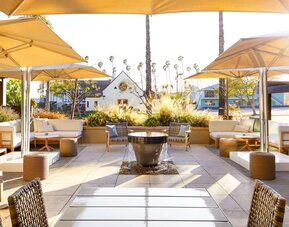 Outdoor patio with lounge seating, umbrellas, fire pit, and landscaped surroundings in soft daylight at The Ambrose Hotel Santa Monica.