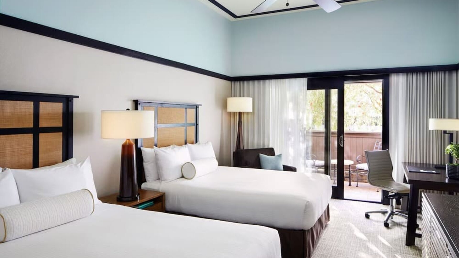 Guest room with two beds, work desk, balcony access, and neutral-toned decor at The Ambrose Hotel Santa Monica.