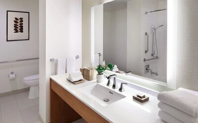 Accessible bathroom with wide vanity, grab bars, walk-in shower, and bright lighting at The Ambrose Hotel Santa Monica.