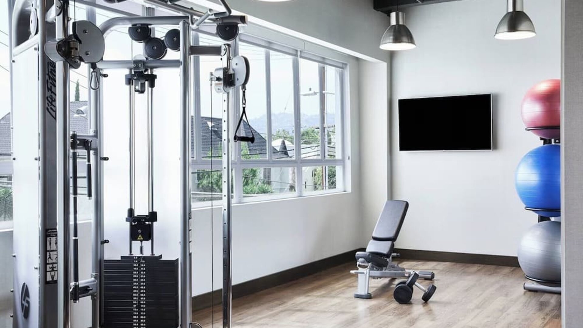 Fitness center with weight machine, bench, exercise balls, and large windows letting in natural light at AC Hotel By Marriott Beverly Hills.