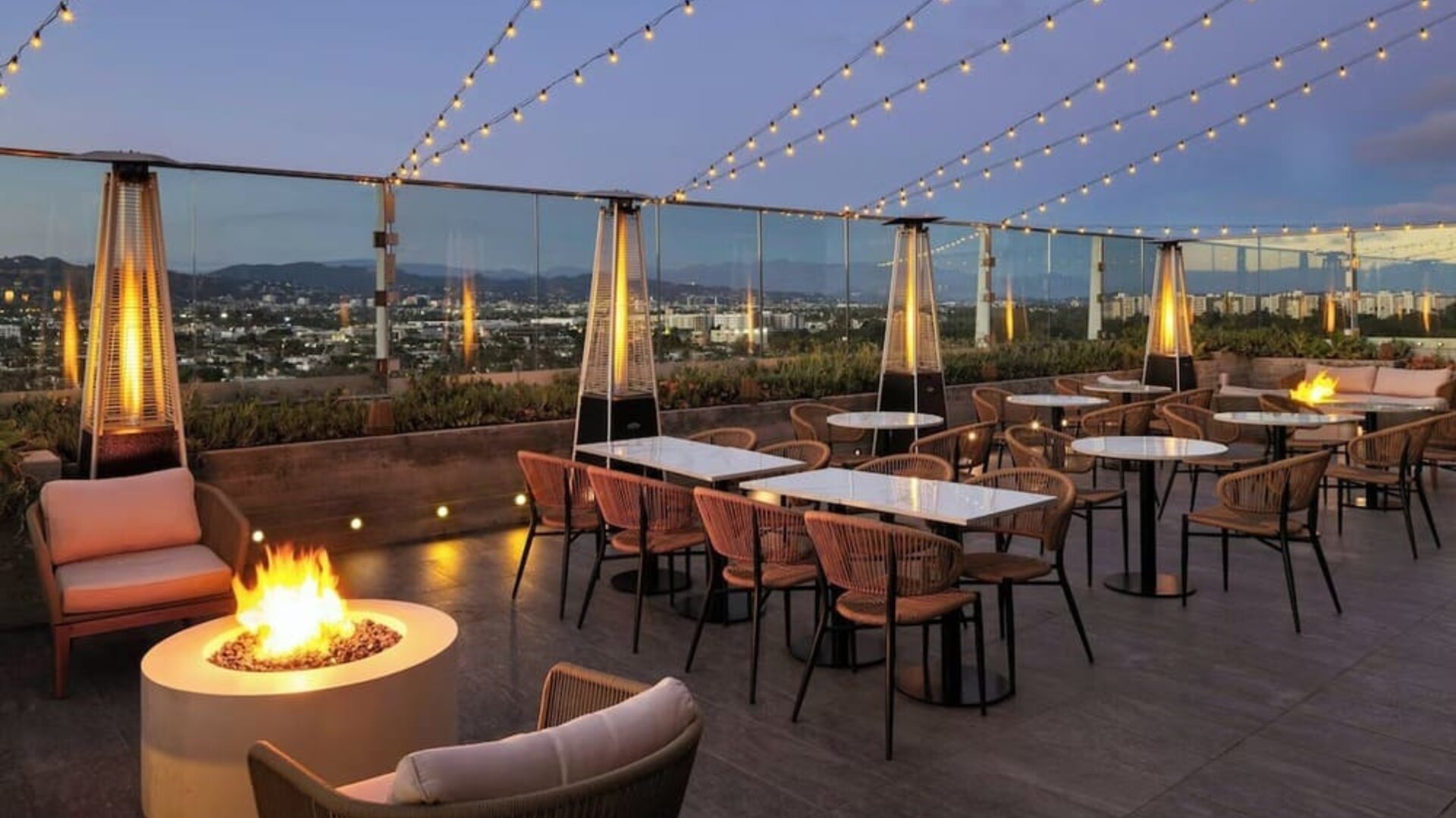 Rooftop terrace with seating, fire pits, string lights, and city skyline views at dusk at AC Hotel By Marriott Beverly Hills.