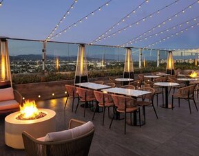 Rooftop terrace with seating, fire pits, string lights, and city skyline views at dusk at AC Hotel By Marriott Beverly Hills.