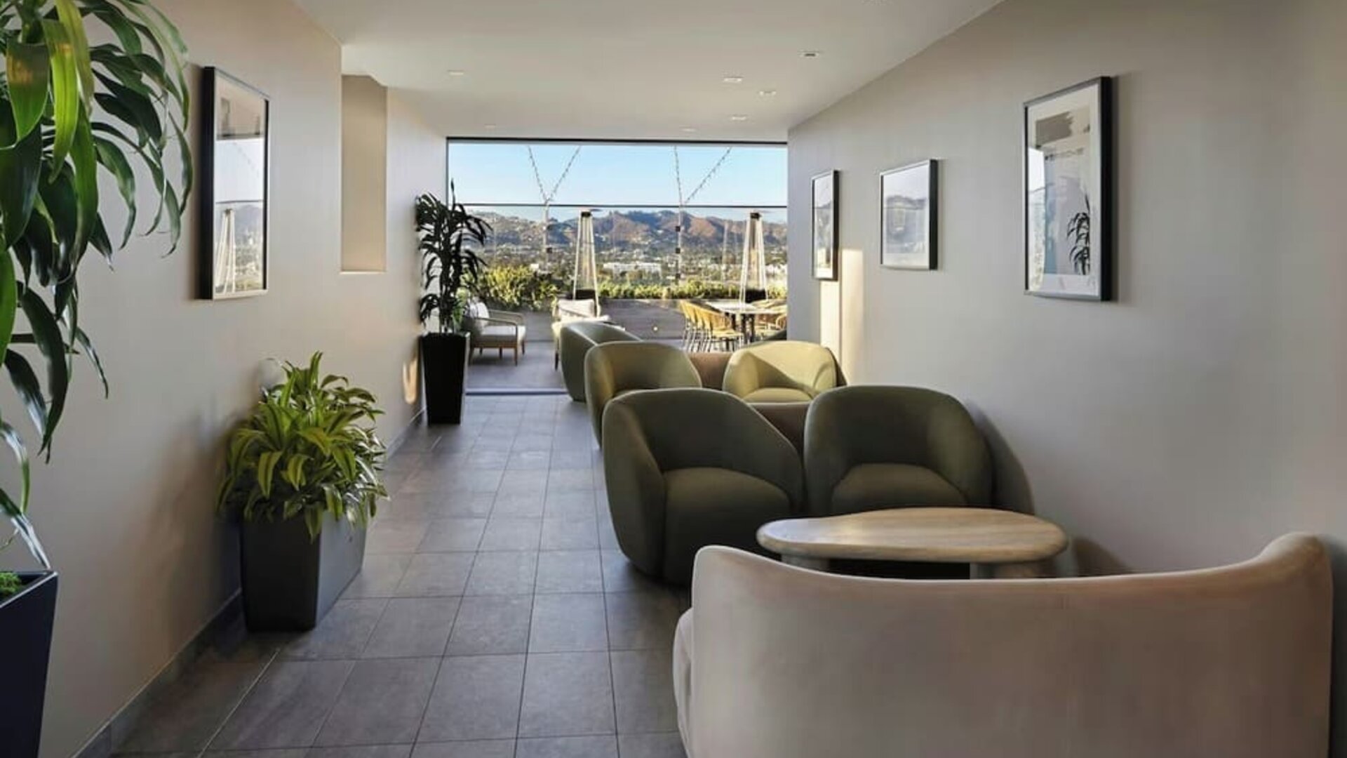 Lounge corridor with cushioned seating, small tables, plants, and open view toward outdoor terrace at AC Hotel By Marriott Beverly Hills.