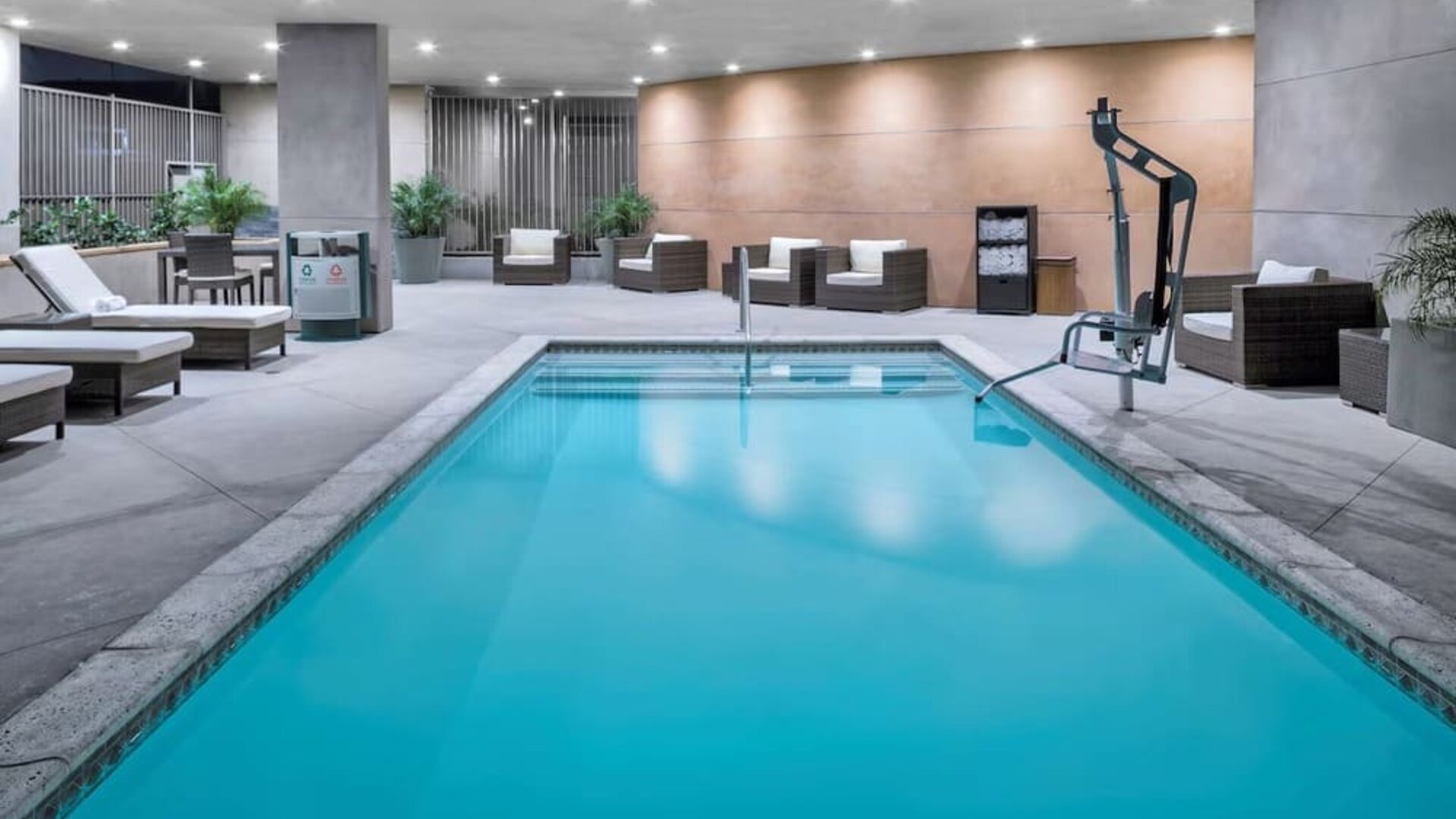 Indoor pool area with seating, accessibility lift, and ambient lighting at Hampton Inn & Suites Los Angeles / Hollywood.
