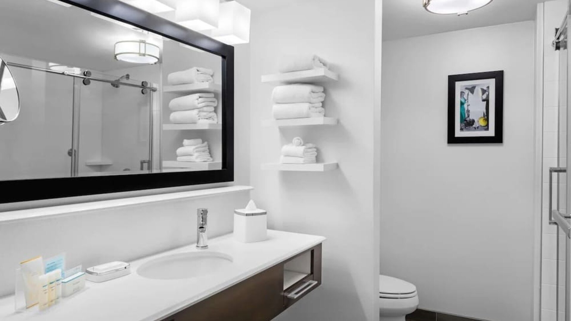 Clean bathroom with large vanity, illuminated mirror, glass shower, and neatly arranged towels at Hampton Inn & Suites Los Angeles / Hollywood.