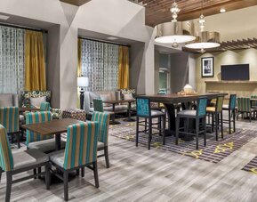 Dining/lounge area with patterned chairs, communal tables, warm lighting, and contemporary décor at Hampton Inn & Suites Los Angeles / Hollywood.