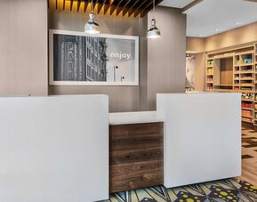 Reception desk area with modern design, wood accents, and small retail/snack section at Hampton Inn & Suites Los Angeles / Hollywood.