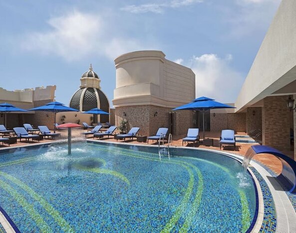 Outdoor pool with blue loungers, umbrellas, water features, and surrounding terrace seating