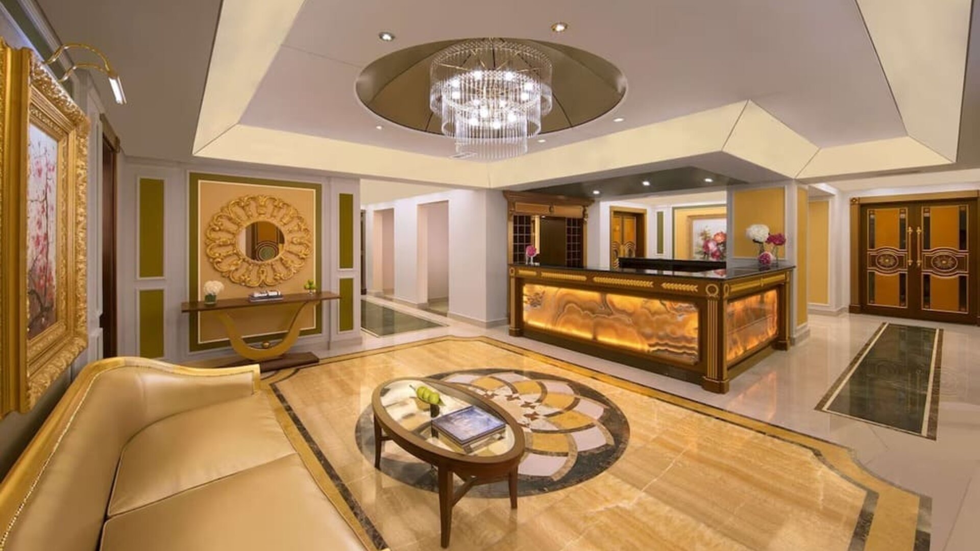 Reception area with curved desk, chandelier ceiling feature, and gold-accented décor