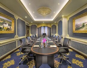 Long conference room with central table, leather chairs, chandeliers, and framed artwork