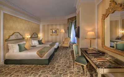 Twin bedroom with two beds, patterned carpet, armchair seating, and wall-mounted television
