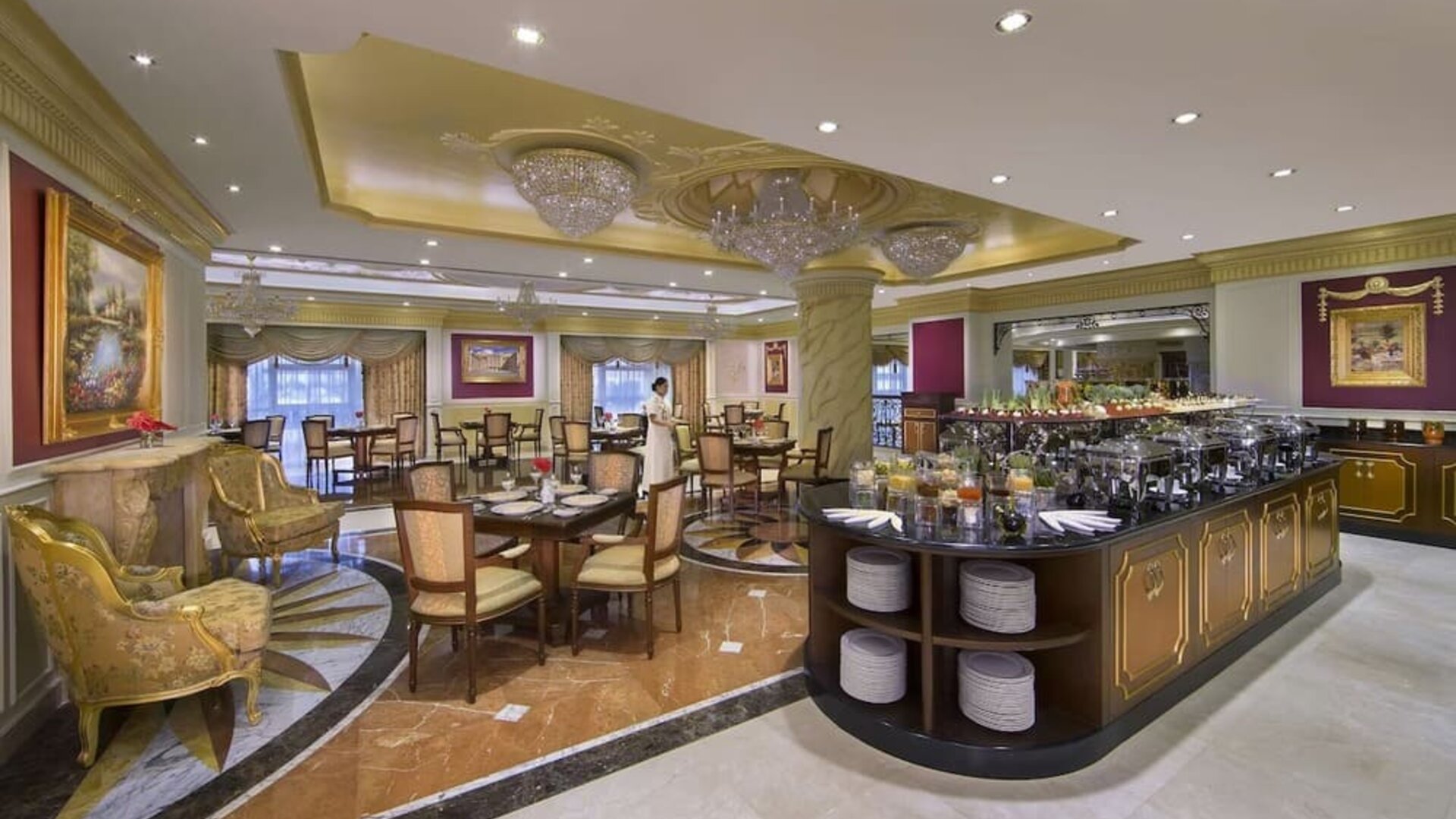 Spacious dining room with buffet station, chandeliers, and multiple tables arranged across marble floors