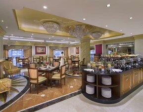Spacious dining room with buffet station, chandeliers, and multiple tables arranged across marble floors