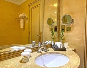 Marble bathroom vanity with round sink, large mirror, toiletries tray, and warm gold-toned finishes