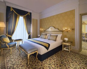 Classic bedroom with blue drapes, upholstered bench, and ornate furniture beside a large bed