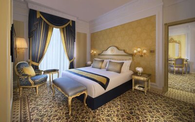 Classic bedroom with blue drapes, upholstered bench, and ornate furniture beside a large bed