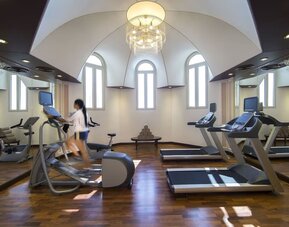 Bright fitness room with treadmills, elliptical machines, mirrored walls, and arched windows overhead