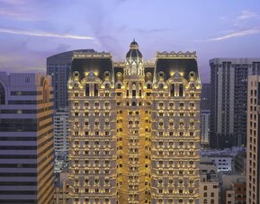 Illuminated multi-story hotel exterior at dusk with ornate façade and surrounding city buildings