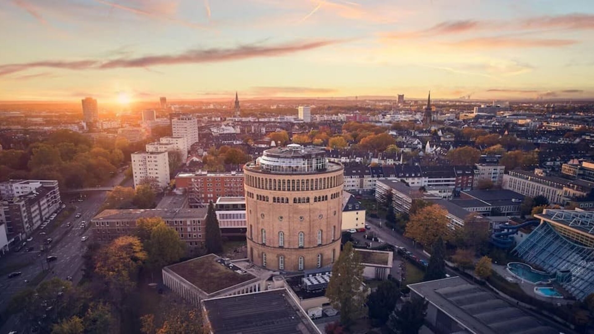 Aerial city view at sunset with round tower building centered among residential blocks and tree-lined streets
