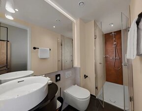Modern bathroom with double sinks, large mirror, walk-in shower, and wall-mounted toilet