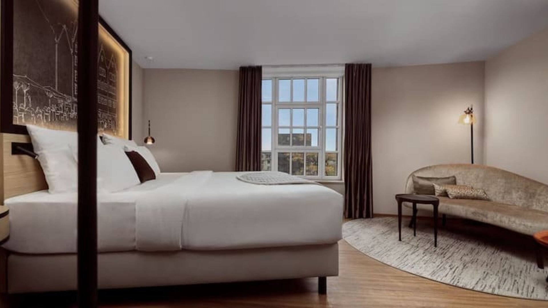 Bright guest room with king bed, curved sofa, round table, and large window with natural daylight