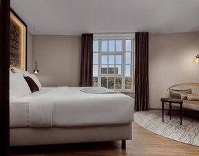 Bright guest room with king bed, curved sofa, round table, and large window with natural daylight