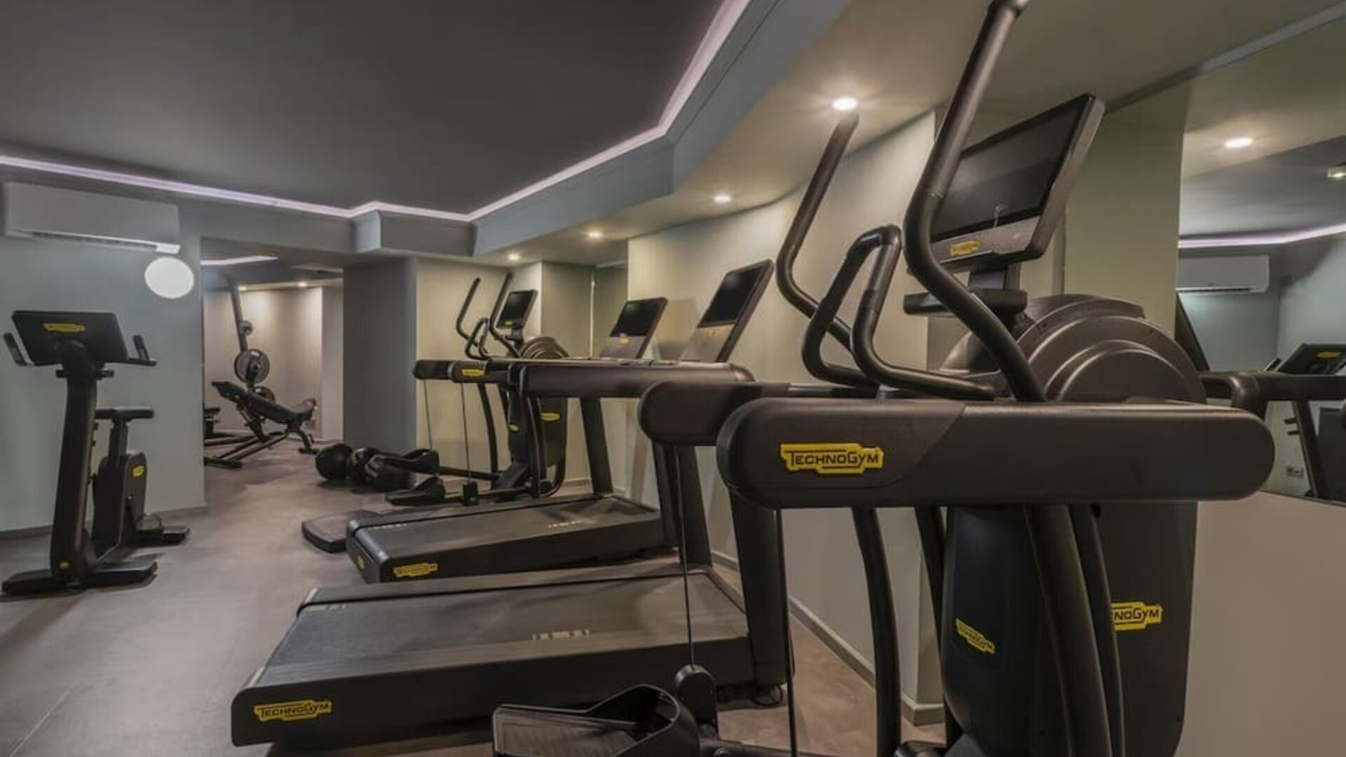Compact fitness room with treadmills, elliptical machines, mirrors, and overhead recessed lighting