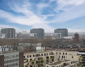 Elevated city view with modern buildings, rooftops, and cloudy sky stretching across the skyline