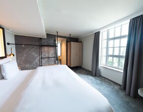 Minimalist bedroom with king bed, gray accent wall, wardrobe, and large window with curtains drawn aside