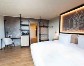 King bed with white linens, wall art headboard, and narrow windowed corridor leading to separate seating area