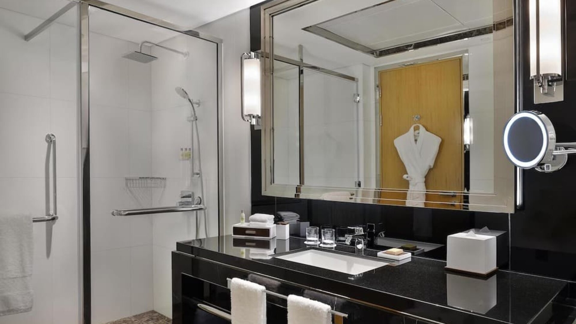 Modern bathroom with glass walk-in shower, black vanity, large mirror, and neatly arranged amenities