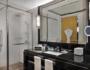 Modern bathroom with glass walk-in shower, black vanity, large mirror, and neatly arranged amenities
