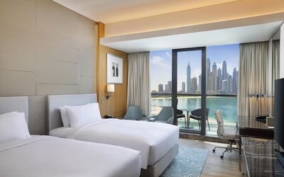 Twin bed guest room with floor-to-ceiling window, balcony seating, and waterfront skyline view