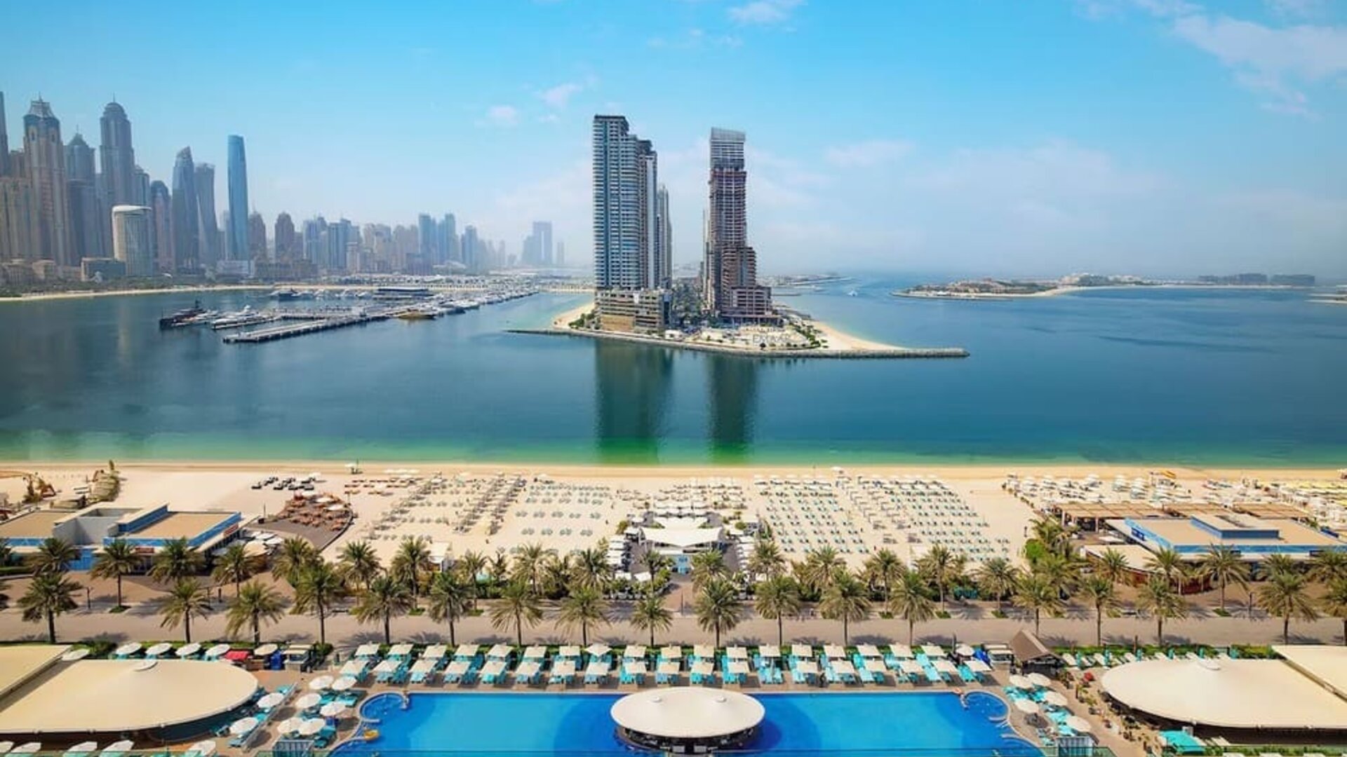 Elevated view of beach, marina, and high-rise skyline with rows of loungers and calm blue water