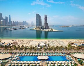 Elevated view of beach, marina, and high-rise skyline with rows of loungers and calm blue water
