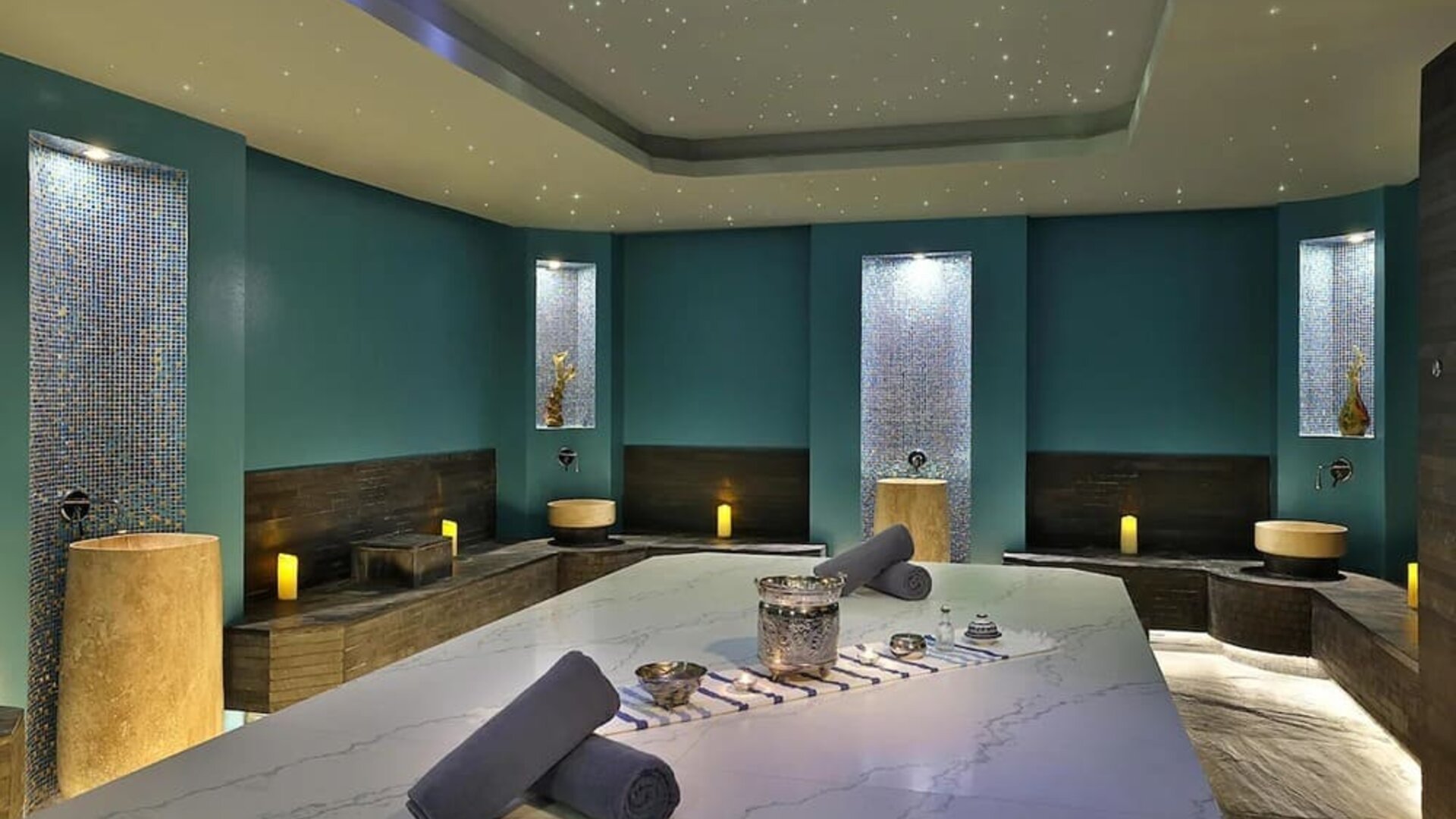 Spa treatment room with massage table, candles, mosaic tile walls, and soft ambient lighting
