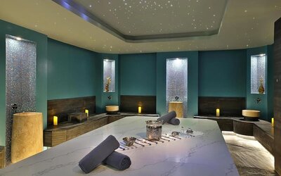 Spa treatment room with massage table, candles, mosaic tile walls, and soft ambient lighting