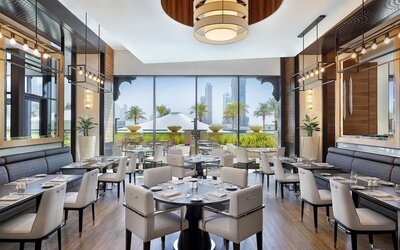 Restaurant dining room with upholstered chairs, pendant lights, and floor-to-ceiling windows to terrace