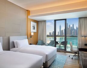 Twin bed guest room with balcony, seating area, and clear view of water and skyline through glass doors