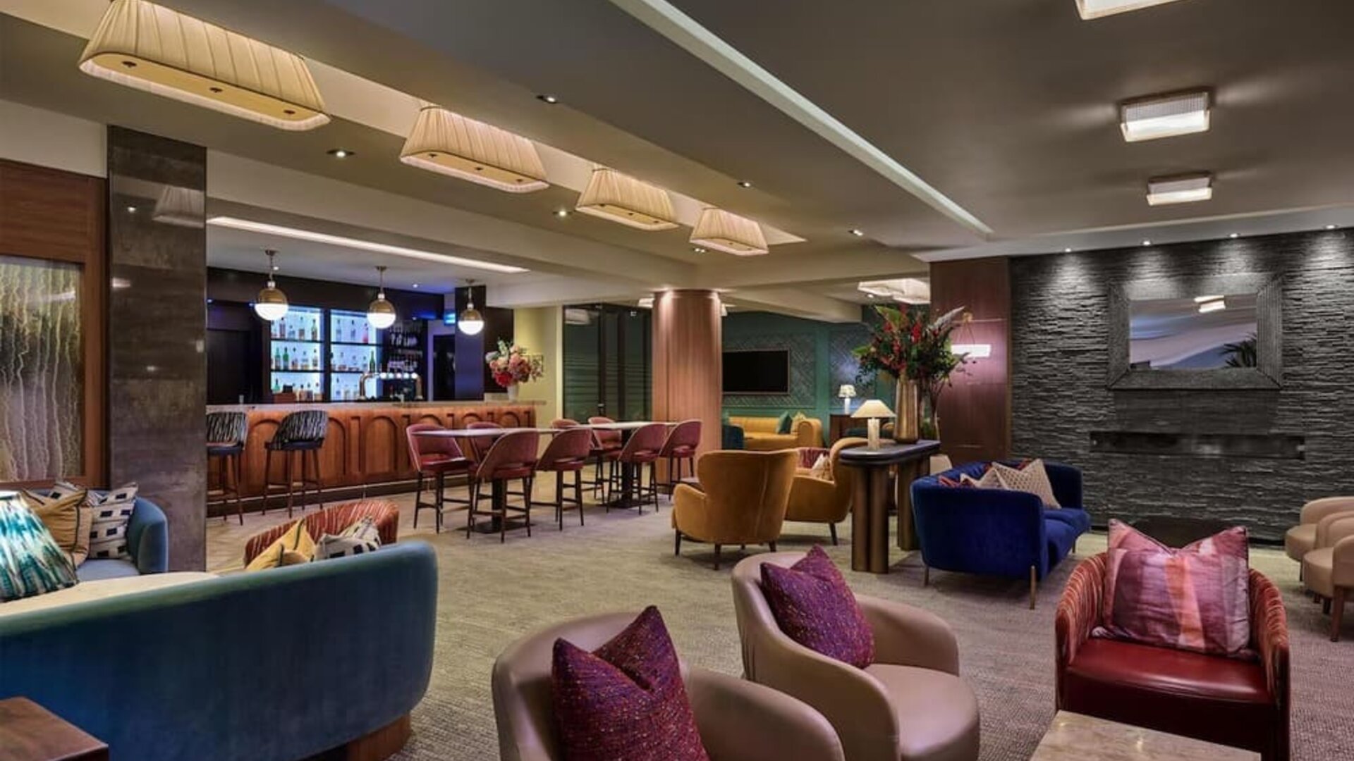 Lounge with colorful armchairs, bar seating, and warm lighting creating a relaxed social atmosphere