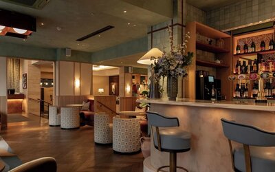 Hotel bar lounge with marble counter, upholstered stools, floral centerpiece, and warm lighting