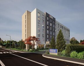 Modern seven-story hotel exterior with landscaped entrance, roadside sign, and trees at dusk