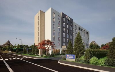 Modern seven-story hotel exterior with landscaped entrance, roadside sign, and trees at dusk