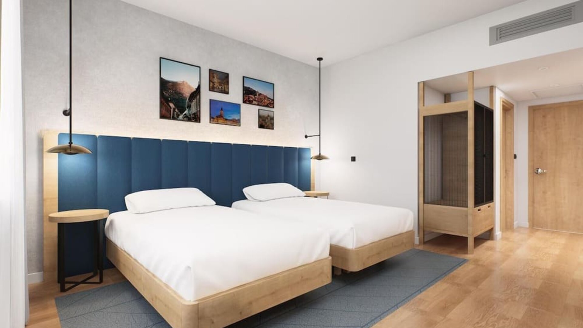 Guest room with two beds, blue padded headboard, wood furniture, and framed wall artwork
